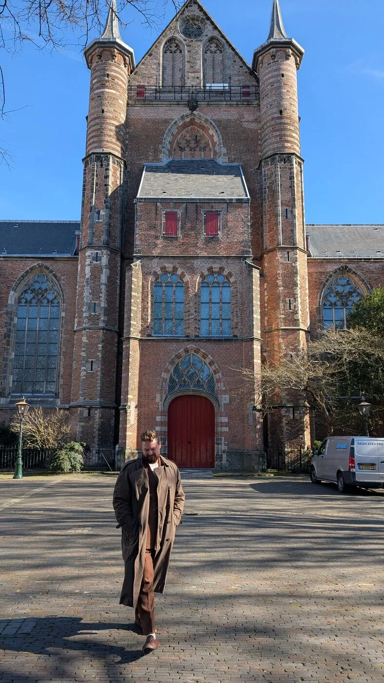 Walking toward the camera, head down, a Gothic church towering behind.